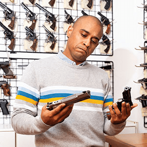 Man Deciding Between Two Pistols at a Gun Store