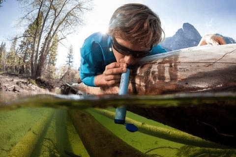Man Using Lifestraw Portable Water Filter to Drink From River
